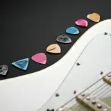 Kolorowe kostki do gitary elektrycznej leżą obok białej gitary. Zastanawiasz się, jak nastroić gitarę elektryczną? Zacznij od wyboru odpowiedniej kostki!
