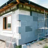Budowa domu z bloczków betonowych, trwa montaż ścian zewnętrznych. Okna już osadzone, trwa praca nad elewacją.