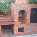 Solidny grill z cegły szamotowej, z kamiennym łukiem nad paleniskiem i metalowymi drzwiczkami. Idealny do ogrodu.