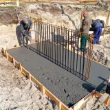 Budowa fundamentów: pracownicy wylewają beton na zbrojenie, tworząc solidny żelbeton.