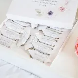 Otwarty biały kartonik z czekoladkami w ozdobnych papierkach, z motywem kwiatowym.