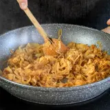Omas Zwiebelrostbraten wird in der Pfanne zubereitet. Zwiebeln werden goldbraun gebraten, ein köstlicher Duft liegt in der Luft.