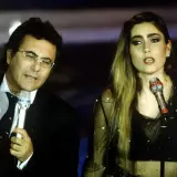 Al Bano i jego nowa partnerka na scenie, w blasku świateł, śpiewają do mikrofonów.