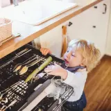 Małe dziecko próbuje sięgnąć do szuflady ze sztućcami. Pomyśl, jak zabezpieczyć szuflady przed dzieckiem domowe sposoby, zanim dojdzie do niebezpieczeństwa.