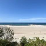 Szeroka, piaszczysta plaża w Jarosławcu, z łagodnymi falami Bałtyku i zielenią w tle. Idealne miejsce na relaks i podziwianie widoków, oferujące liczne atrakcje.