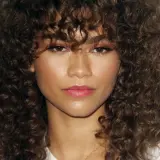 Zendaya mit voluminösen, braunen Locken, die ihr Gesicht umrahmen. Eine Inspiration für Frisuren mit Locken.