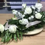 Białe róże na drewnianym stole, ozdobione wstęgą. Biała róża symbolizuje czystość i niewinność, często wybierana na uroczystości.