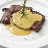 Un steak grillé, nappé d'une sauce crémeuse et garni d'une branche de romarin. Parfait pour accompagner une sauce pour entrecôte au barbecue.