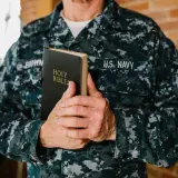 Marynarz w mundurze U.S. Navy trzyma Biblię. W jego dłoniach spoczywa księga, która może zawierać pieśń dawida, symbol wiary i nadziei.