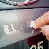 Dłoń usuwa resztki starej naklejki z samochodu, pokazując, jak odkleić naklejkę z samochodu bez śladu.