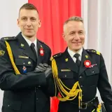 Dwóch mężczyzn w galowych mundurach, z bogatym **uposażeniem**, ściska sobie dłonie.
