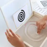 Niño practicando preescritura montessori, trazando espirales en arena.
