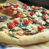 Pyszna pizza ze szpinakiem, pomidorkami koktajlowymi i kostkami sera feta. Idealna na szybki obiad.