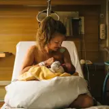 En mamma ammar sitt nyfödda barn på en sjukhussäng. En lugn stund efter förlossningen, kanske inför en efterkontroll på MVC.