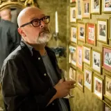 Łysy mężczyzna w okularach ogląda zdjęcia na ścianie. Czy to obsada z "Domu Złego"?