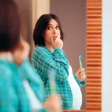 Donna incinta si tocca le labbra, preoccupata per le gengive gonfie in gravidanza. Tiene uno spazzolino, pronta a prendersi cura del suo sorriso.