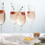 Cztery kieliszki orzeźwiającego prosecco rose z malinami i gałązkami tymianku, gotowe na toast.