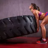 Kobieta w sportowym stroju wykonuje ćwiczenie z ogromną oponą, typowe dla treningu crossfit.