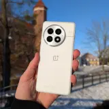 Biały smartfon z charakterystycznym modułem aparatów, trzymany na tle zimowego krajobrazu z zamkiem. System Oxygen OS działa płynnie.
