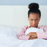 Chica enfadada en la cama, pensando en excusas para no quedar.