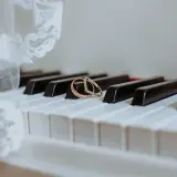 Dwa obrączki na klawiszach pianina, obok białej koronki.