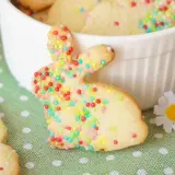 Bunte Osterkekse zum Ausstechen, verziert mit bunten Streuseln, liegen auf einem grünen Tupfentuch. Ein süßer Osterhase steht im Vordergrund.