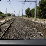 Widok z samochodu na tory kolejowe. W oddali widać budynki i drzewa. To **przejazd kolejowy bez zapór**, gdzie trzeba uważać na pociągi.