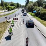 Prace drogowe na linii 101 Szczecin. Robotnicy w kamizelkach odblaskowych przygotowują nawierzchnię, jeden z nich pcha taczkę z materiałem.