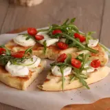 Pyszna focaccia z mozzarellą, pomidorkami koktajlowymi i rukolą, podana na papierze do pieczenia.