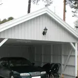 Vit carport på plintar med en bil och barnvagn.