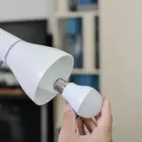 Ręka wymienia żarówkę w lampce biurkowej, symbolizując modernizację oświetlenia i oszczędność energii.