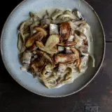 Cremige Spaghetti mit gebratenen Pilzen, ein köstliches italienisches Gericht, serviert in einer rustikalen Schüssel auf dunklem Holz.