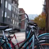 Kilka rowerów, w tym jeden z niebieską ramą i pomarańczowymi obręczami, zaparkowanych przy ulicy. Rozmiar ramy Romet jest idealny na miejskie przejażdżki.