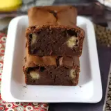 Dos porciones de bizcocho de plátano y chocolate apiladas, con trozos de plátano visibles en su interior.