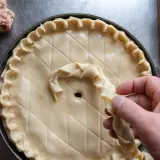 Préparation d'une tarte salée, peut-être une recette joue de porc rapide. Une pâte est décorée avec une tresse.