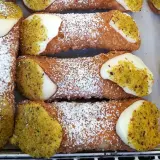 Zbliżenie na sycylijskie cannoli posypane cukrem pudrem i pistacjami, z kremowym nadzieniem.