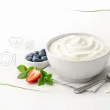 Gładki skyr naturalny w misce, obok jagody, truskawka i listki mięty. Zdrowy posiłek.
