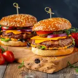 Dwa soczyste burgery z wołowiny, idealne jakie mięso na burgera, z serem, warzywami i piklami na drewnianej desce.