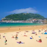 Gente disfrutando de la arena dorada y el mar turquesa en la que podría ser la mejor playa de España, con la ciudad y un monte verde de fondo.