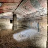 Interno di una tomba etrusca con soffitto dipinto e un pilastro centrale. Un cerchio inciso sul pavimento sembra un antico incantesimo putifigari.