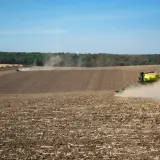 Traktor z siewnikiem na polu, wzbijający tumany kurzu.