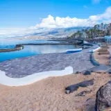 Słoneczna playa de las americas z basenem, piaskiem i kolorowymi budynkami w tle.
