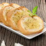 Tranches de pain grillé à l'ail, garnies d'herbes, rappelant la préfou recette traditionnelle. Une tête d'ail repose à côté.