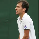 Jerzy Janowicz, z rakietą w dłoni, unosi palec wskazujący, świętując zwycięstwo. Jego majątek rośnie z każdym wygranym meczem.