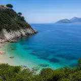 Vue d'une crique aux eaux turquoise cristallines, avec une colline verdoyante et des maisons blanches perchées, près d'une île à côté de Capri.