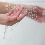 Manos bajo un chorro de agua fría, sintiendo el frescor al ducharse con agua fría.