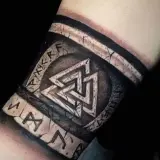 Tatuaż na przedramieniu z nordyckimi symbolami: Valhalla i runy. Wygląda jak starożytny artefakt.