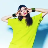 Modelka w limonkowym, luźnym T-shircie i złotych bransoletach, prezentująca najnowszy trend.