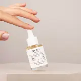 En hand håller en flaska Apoliva Niacinamid Serum. Denna produkt, som innehåller niacinamid och retinol, är utformad för att minska porer och jämna ut hudtonen.