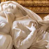 Estasi di Santa Teresa a Roma, marmo bianco su fondo dorato. La santa giace su un cuscino, con un'espressione di profonda emozione.